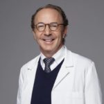 A man in white coat and glasses smiling for the camera.